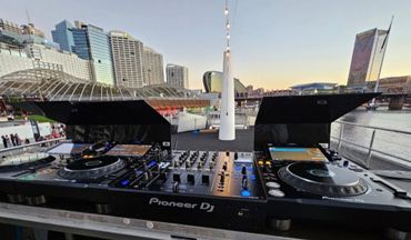 Pioneer DJ equipment set up outdoors with a city skyline in the background.