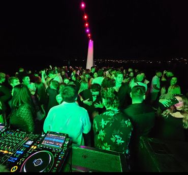 Crowded night party with DJ equipment and colorful string lights.