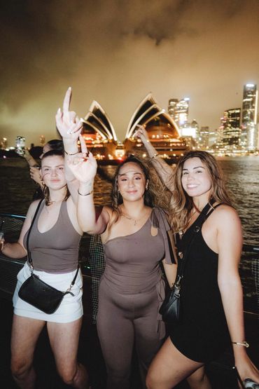 Three women posing happily at night with Sydney Opera House in the background.