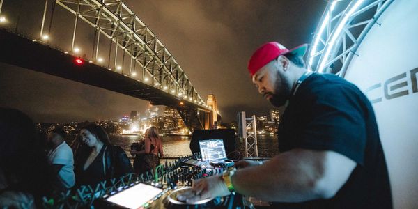 DJ playing music at night near a lit-up bridge with people enjoying the scene.