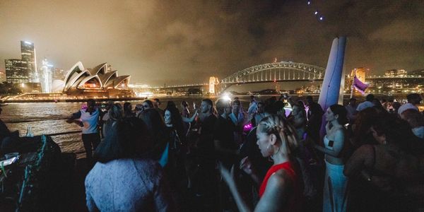 Night party on a boat with Sydney Opera House and Harbour Bridge illuminated in the background.