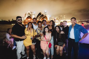 A lively group of friends posing with Sydney Opera House at night.