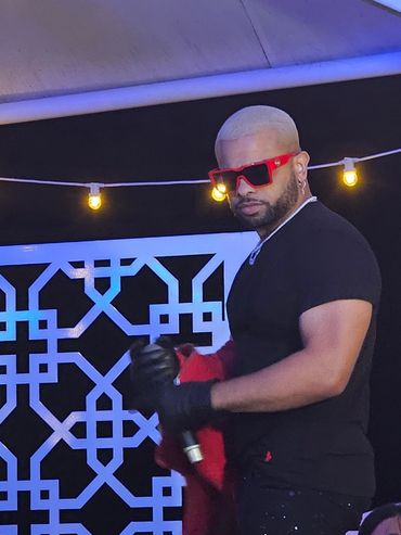 Man with blonde hair and red shades holding a microphone on stage.