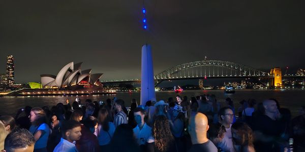 Crowd enjoying a nighttime event with Sydney Opera House and Harbour Bridge in the background.