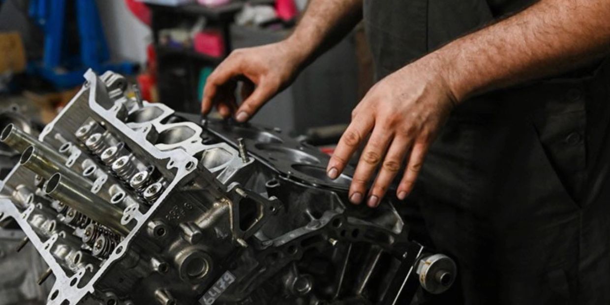 Mechanic assembling a car engine with focused hands in a workshop.