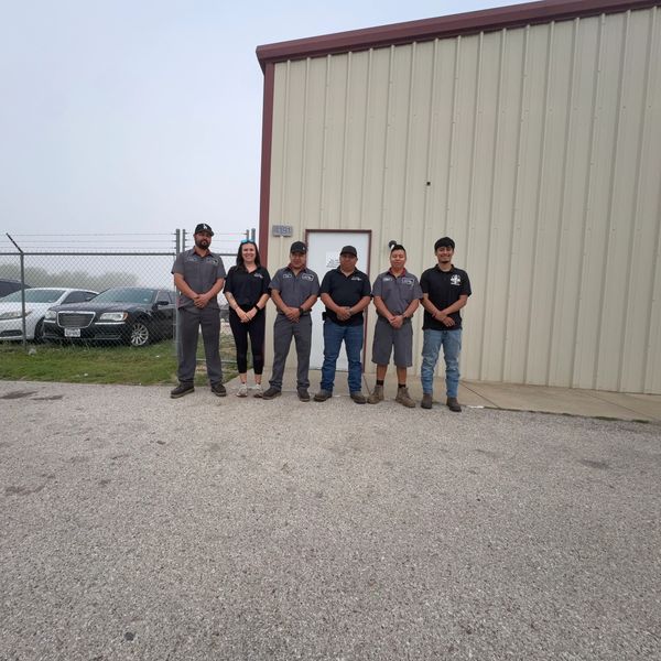 Six people in work uniforms standing outside an industrial building.