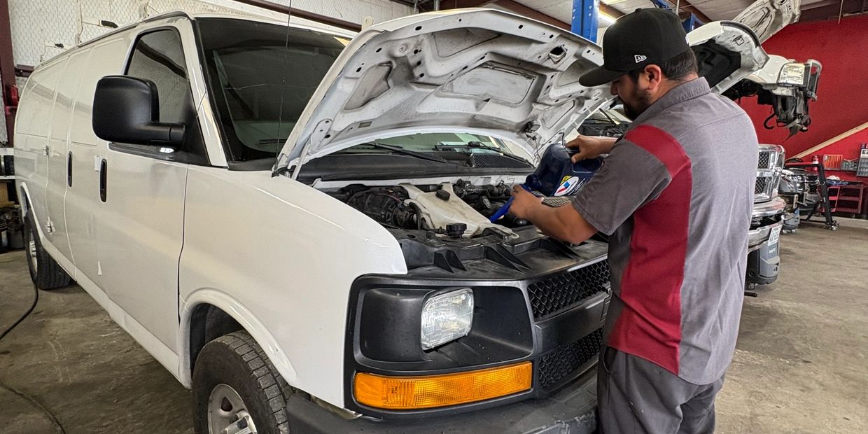Mechanic pouring oil into a white van's engine in a garage.