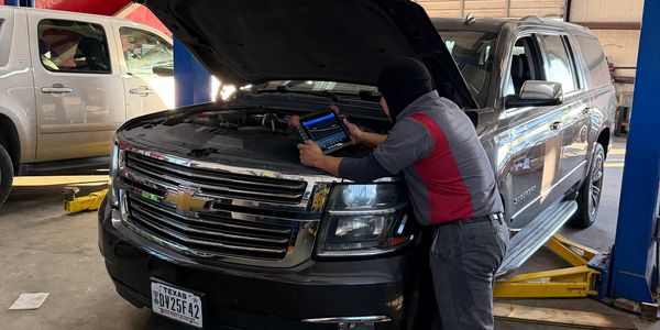 Mechanic using diagnostic tool on a black Chevrolet SUV in a garage.