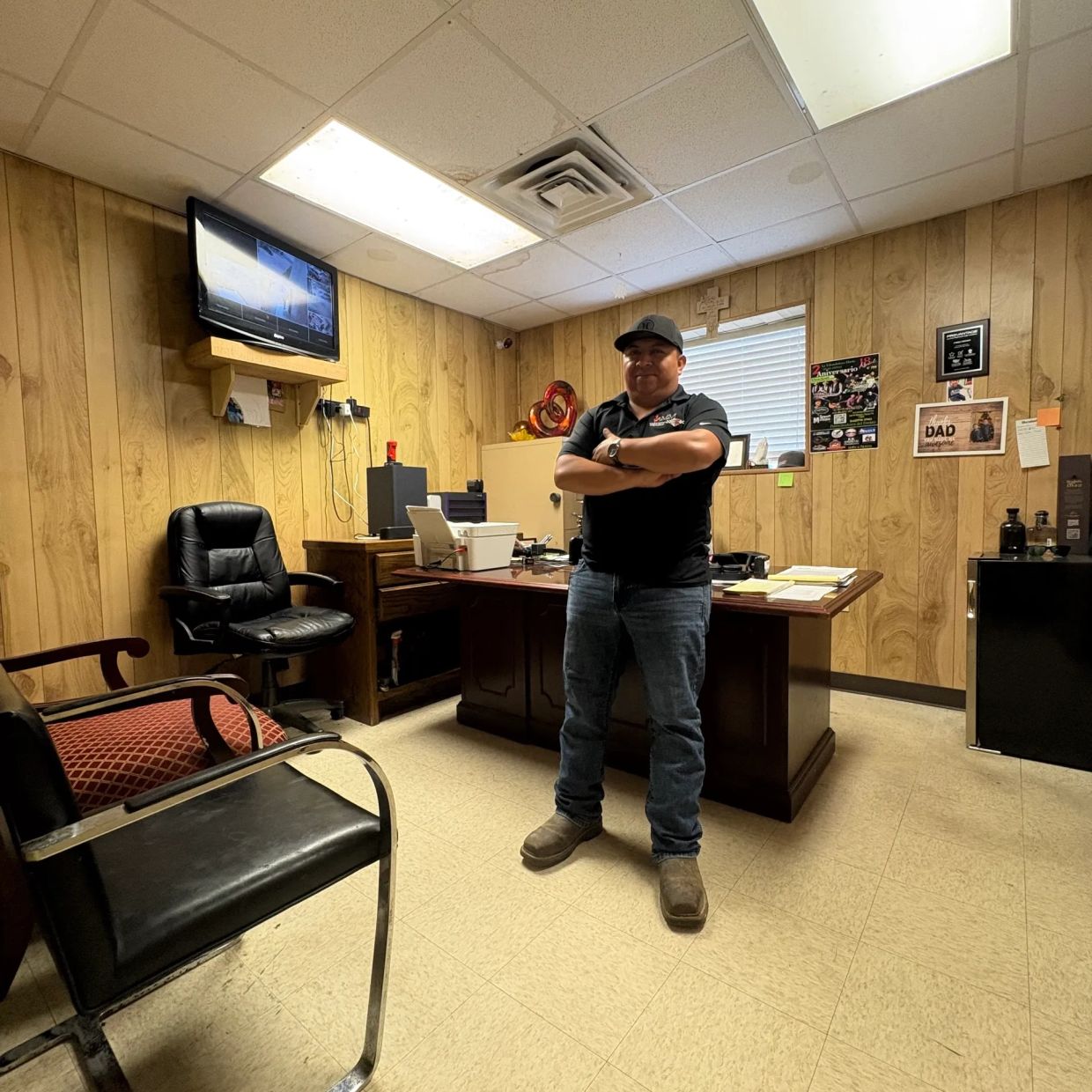 Man standing confidently in a wood-paneled office with crossed arms.