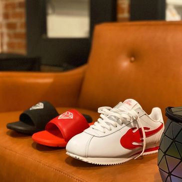 White sneaker with red flame design and two slide sandals on a brown leather couch.