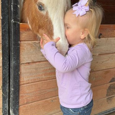 Little girl nuzzling pony.