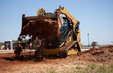 A CAT skid steer loader moving a pile of dirt at a construction site.