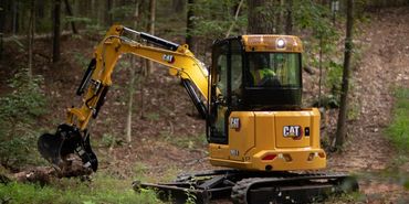 Yellow CAT excavator working in a forest clearing.