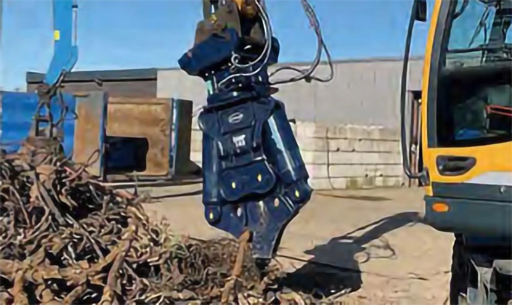 Hydraulic excavator attachment breaking debris at construction site.