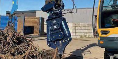 Excavator with hydraulic shear attachment cutting scrap metal outdoors.