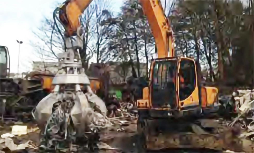 Excavator with claw attachment lifting scrap metal in a scrapyard.