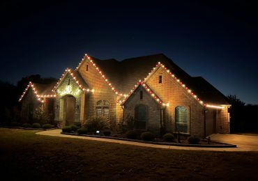 Brick house decorated with red and white Christmas lights at night.