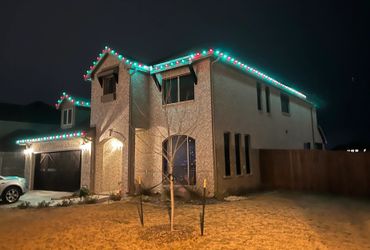 Two-story brick house decorated with red and green Christmas lights at night.