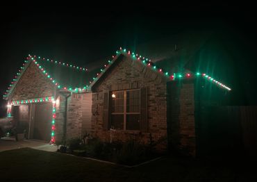 Brick house decorated with red and green Christmas lights at night.