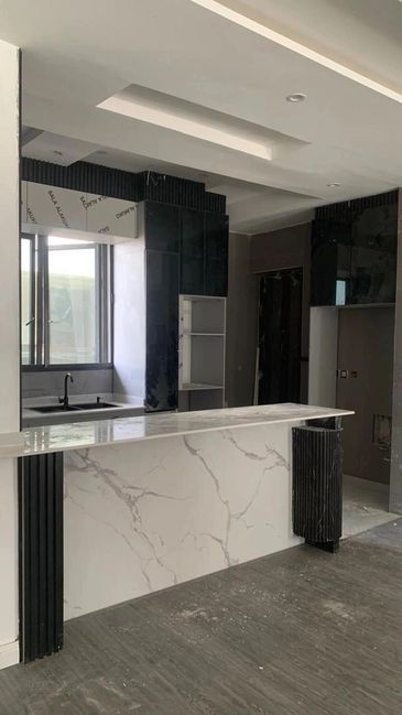 Modern kitchen with marble island and black cabinets under construction.