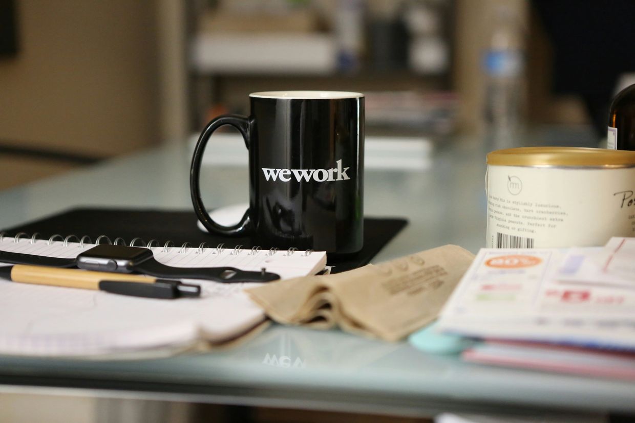 Black WeWork mug on a cluttered desk with office supplies.