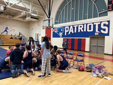 Youth wrestling team huddles in gym with 'Patriots' mural on wall.