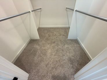 Empty walk-in closet with beige carpet and hanging rods on both sides.