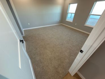 Empty room with beige carpet and gray walls lit by natural light.