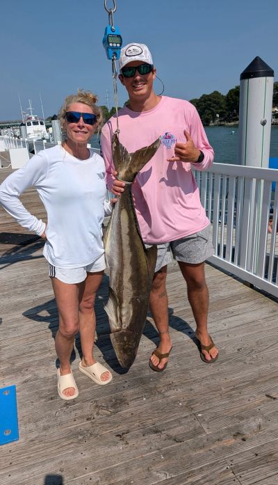 Two people proudly displaying a large fish caught at a dock.
