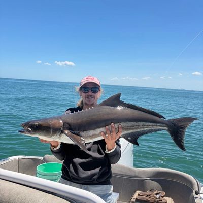 Person proudly holding a large fish on a boat with the ocean in the background.