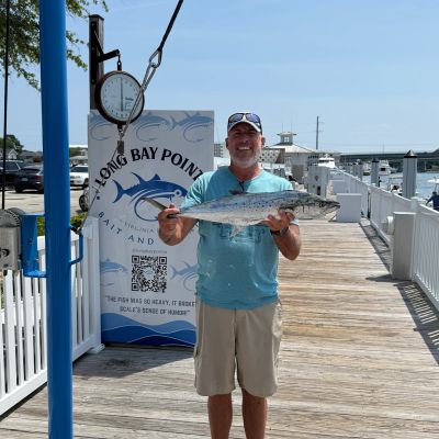 Man proudly holding a freshly caught fish on a sunny dock.