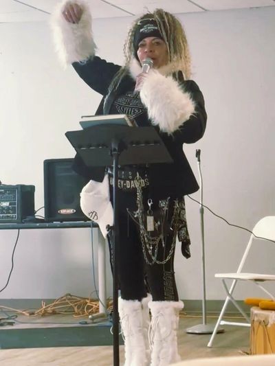 Person with microphone and unique outfit speaking indoors.