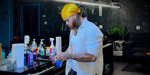 A tattooed man in a yellow bandana prepares supplies in a tattoo studio.