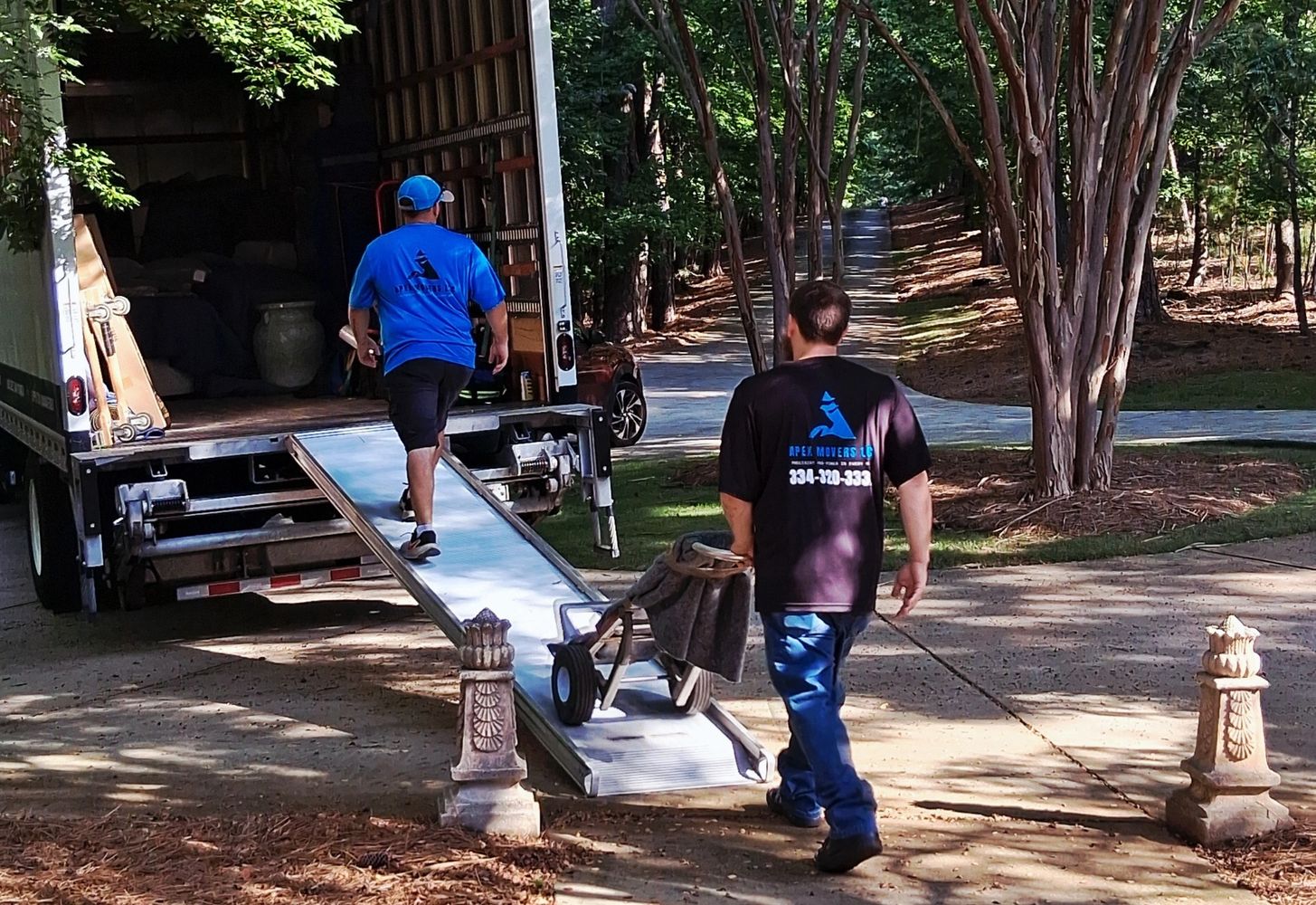 Two movers unloading a truck in a wooded area.