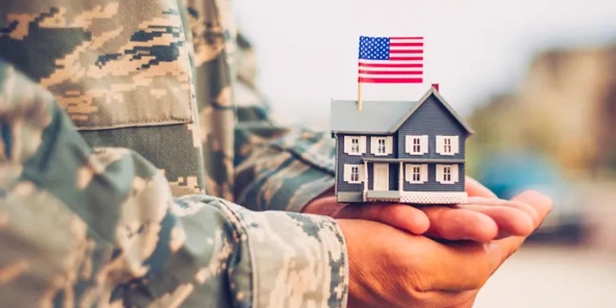 A soldier holds a miniature house with an American flag on top.