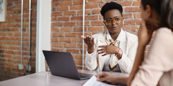 Dua wanita berdiskusi di meja dengan laptop.