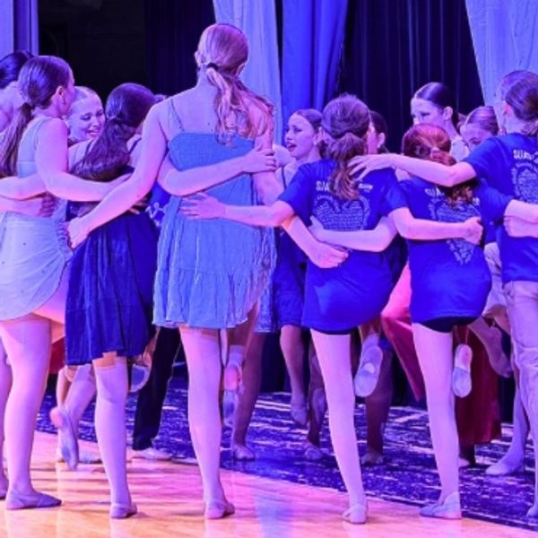 Group of young dancers embracing on stage.
