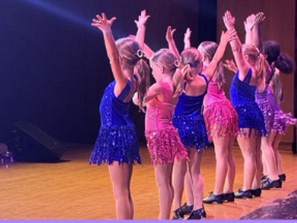 Young girls performing a dance on stage in colorful costumes.