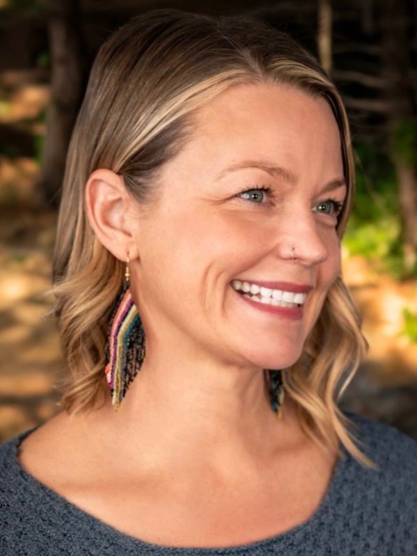 Smiling woman with blonde hair wearing colorful earrings and a blue top.
