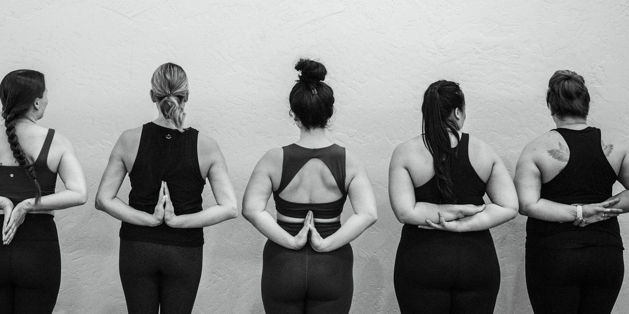 Five women practicing yoga with hands in reverse prayer pose against a textured wall.