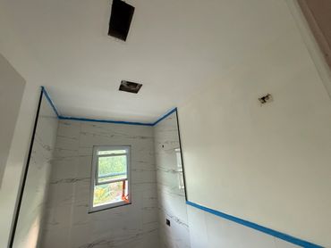 A bathroom under renovation with marble wall tiles and blue painter's tape.