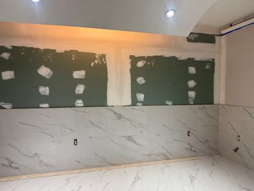 Partially tiled bathroom wall with drywall patches and recessed lighting.