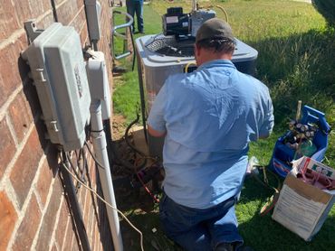 Technician repairing an outdoor air conditioning unit beside a brick wall.