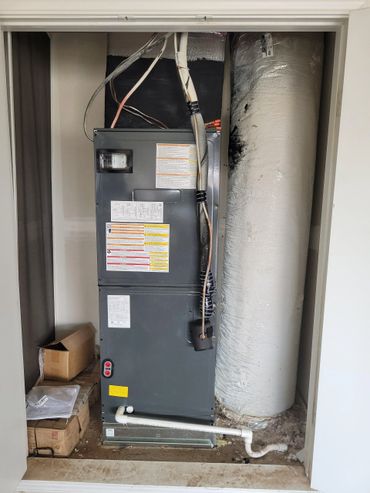 HVAC unit installed in a small utility closet with connected pipes and ducts.