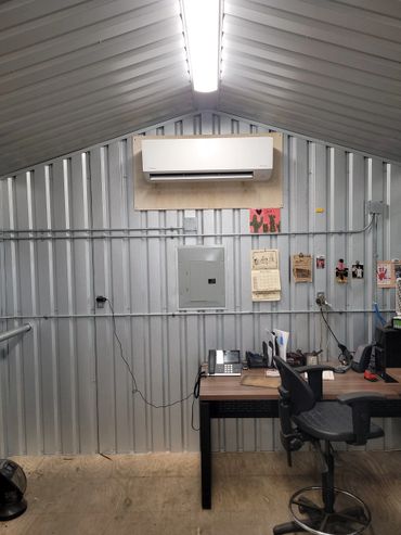 Industrial office space with metal walls, an air conditioner, and a cluttered desk.