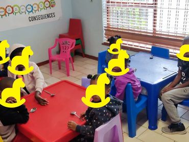 Children sitting at colorful tables in a classroom setting.