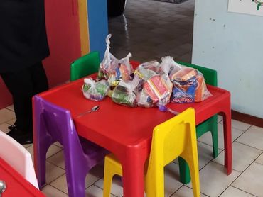 Colorful children's table with snacks in plastic bags and small chairs in a classroom.