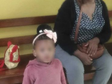 A woman sitting on a bench with a young girl standing beside her.