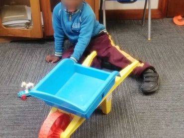 A child playing on the floor with a colorful toy wheelbarrow indoors.