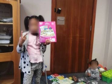 Two children playing with books and toys in a room with a wooden door.